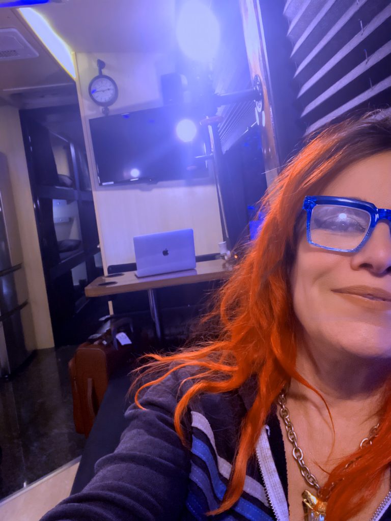 Jennifer Finch May 2024, May Daze Tour with L7 on a tour bus, red hair blue glasses