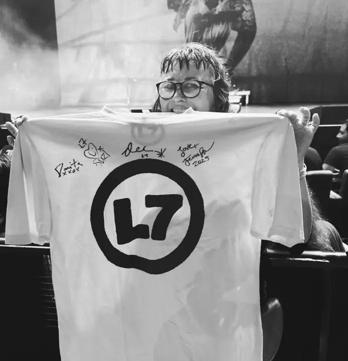 Woman holding up an autographed white L7 t-shirt.