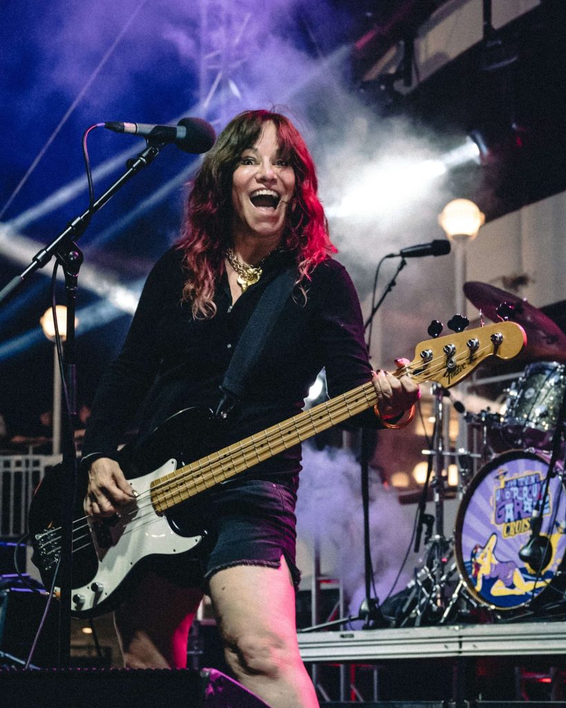Jennifer Finch performing with a bass on stage while smiling for the camera.